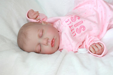 A baby doll resting on a neatly made bed, surrounded by soft blankets and pillows.